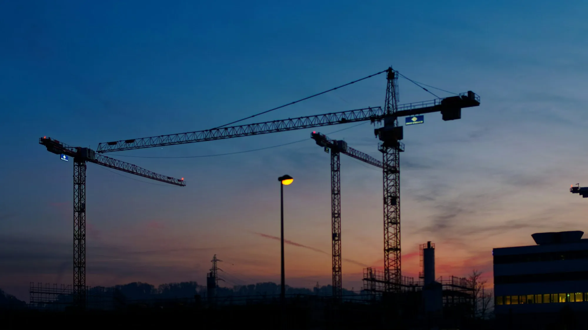 Baukräne vor dem Abendhimmel über einer Großbaustelle