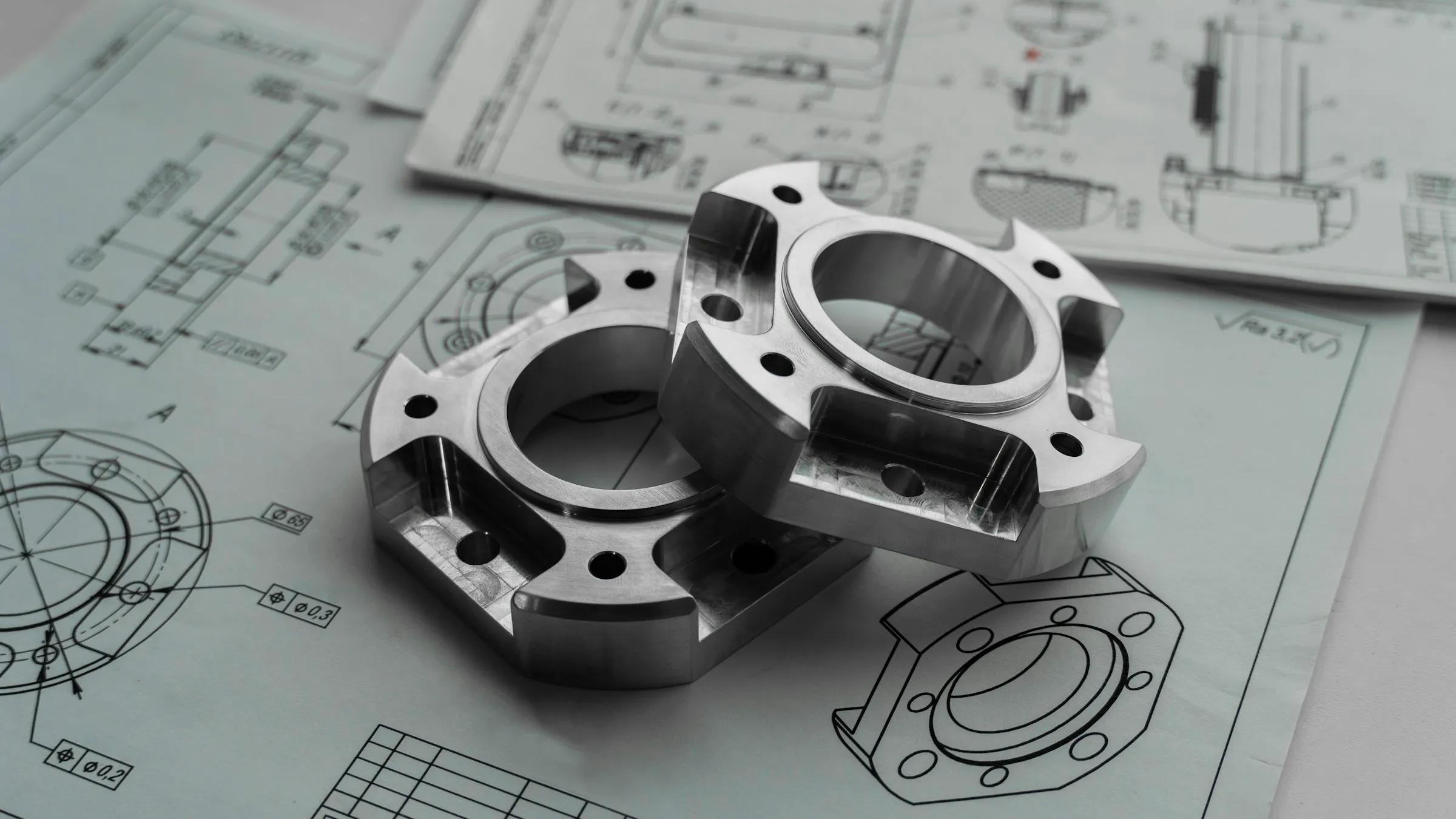 Zwei präzise gefräste Aluminiumteile auf technischen Zeichnungen