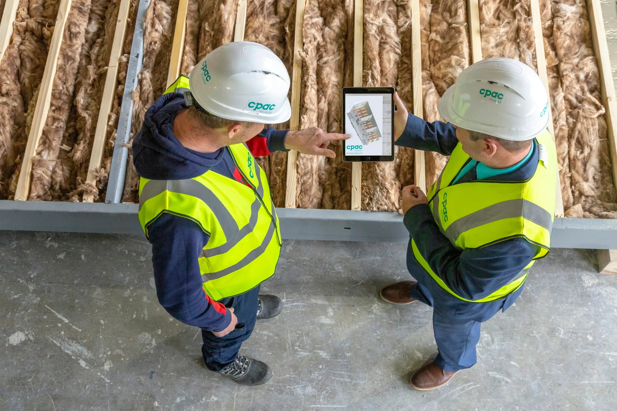 Zwei Bauarbeiter in Warnwesten besprechen einen Plan auf einem Tablet