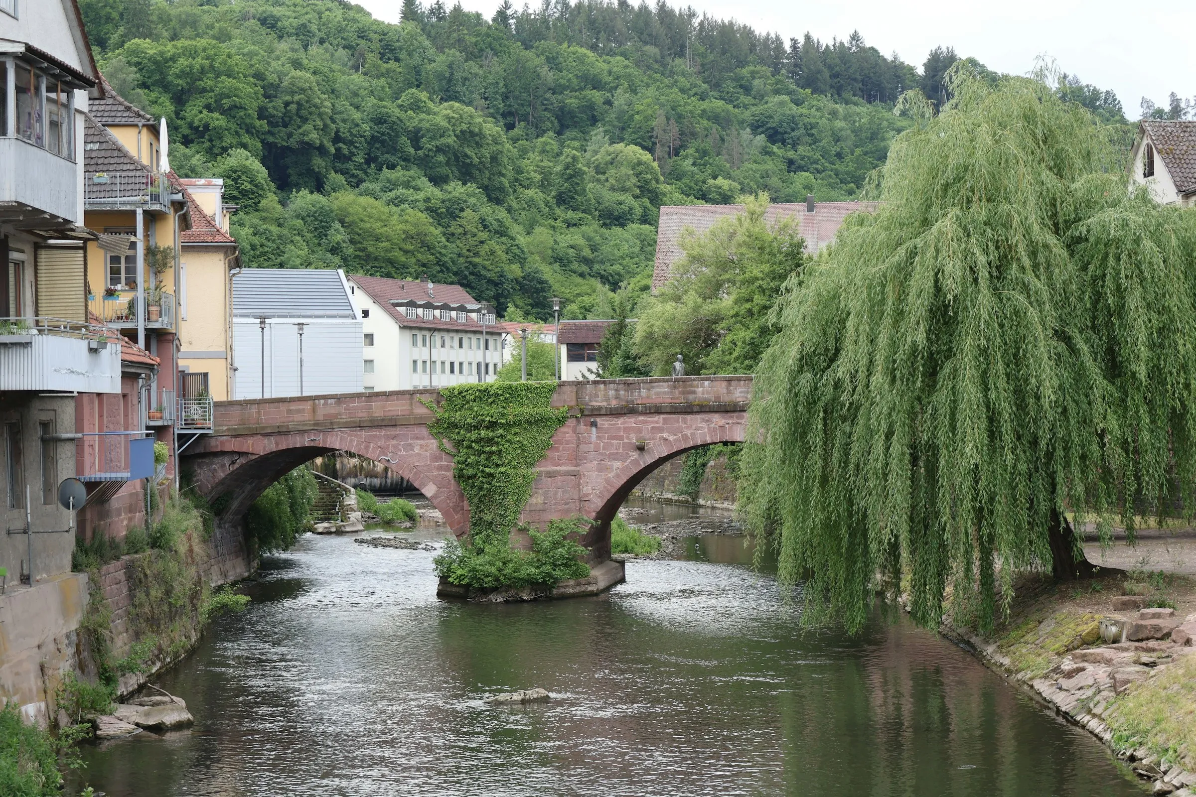 Alte Sandsteinbrücke über die Nagold in Calw, dahinter bewaldete Hänge