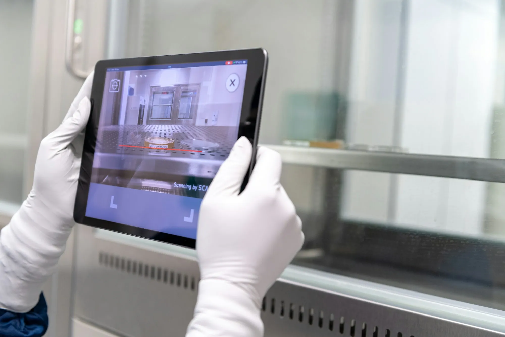 Hände in Arbeitshandschuhen halten ein Tablet in einer Produktionshalle
